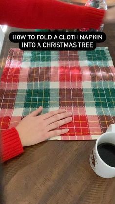 a woman's hand resting on a plaid cloth next to a cup of coffee