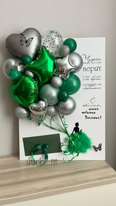 a bunch of green and silver balloons on top of a wooden table next to a card