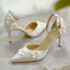 a pair of white high heels with flowers on the toe and ankle straps, sitting on a lace tablecloth