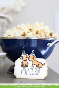 a blue bowl filled with popcorn sitting on top of a counter next to a sign that says pup corn