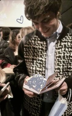 a man in a jacket and bow tie looking at an open book while standing next to other people