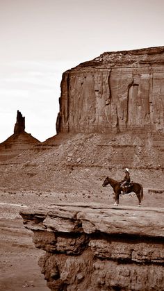 a man riding on the back of a brown horse across a desert land covered in dirt