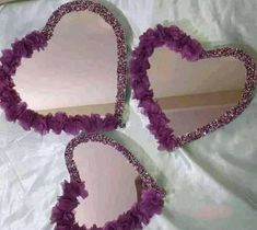 three heart shaped mirrors sitting on top of a white cloth covered tablecloth with purple flowers in the shape of hearts