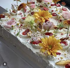 a cake with white frosting and lots of flowers on the top is sitting on a table