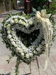 a heart - shaped wreath with white flowers and greenery is placed on a stand