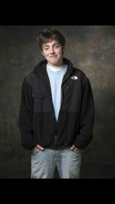 a young man standing in front of a black background with his hands in his pockets