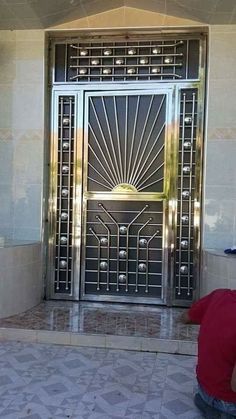 a man sitting on the ground in front of a metal door with an intricate design