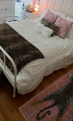 a white bed with leopard print pillows and blankets on it's headboard in a bedroom