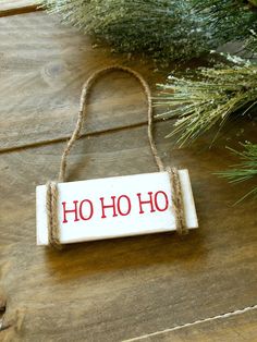 a wooden sign that says ho ho on it hanging from a rope next to a pine tree