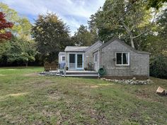 a small gray house sitting on top of a lush green field next to a forest