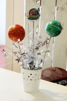 a vase filled with assorted bowling balls on top of a white table next to a wall