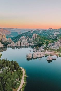 an aerial view of the lake surrounded by rocks and trees at sunset or sunrise with mountains in the background