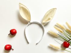 a white bunny ears headband next to some red berries and grass on a white surface