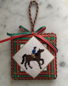 a cross stitch ornament with a horse on it's back hanging from a red ribbon