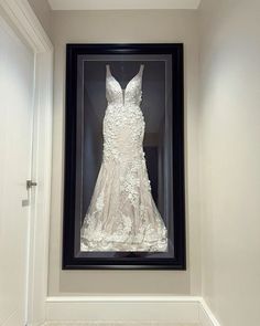 a wedding dress is displayed in a black and white shadow frame on the wall next to a door