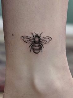 a small bee tattoo on the side of a woman's foot, it is black and white