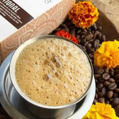 a cup of coffee sitting on top of a table next to some flowers and beans