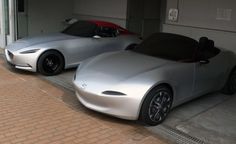 two silver sports cars parked next to each other in front of a garage with doors open