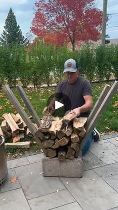 a man sitting on the ground next to a pile of firewood in front of a trash can