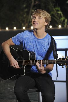 a young man playing an acoustic guitar with a quote from hero on the back ground