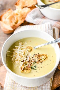 there is a bowl of soup with noodles and cheese on the table next to bread