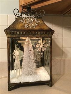 an old fashioned lantern is decorated with snow and christmas decorations, including a white tree