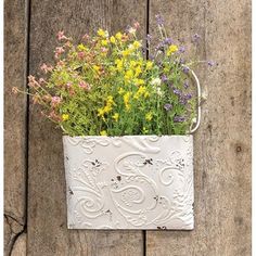 a white metal planter filled with wildflowers on top of a wooden fence