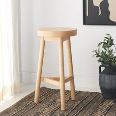 a wooden stool next to a potted plant in front of a painting on the wall