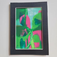 an abstract painting with green, pink and blue colors in a black frame on a white wall