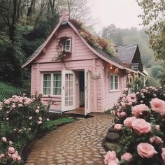 a small pink house in the middle of flowers and greenery, with a pathway leading to it