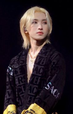 a woman with blonde hair wearing a black jacket and yellow scarf over her shoulders, looking off to the side