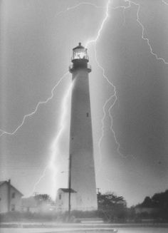 a black and white photo of a lighthouse with lightning in the background