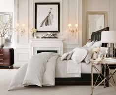 a bedroom with white bedding and chandelier above the fireplace in front of it