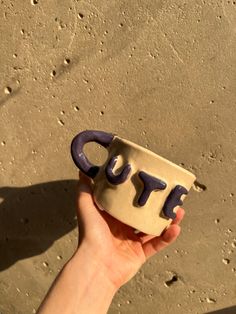 a hand holding a ceramic cup with the word joy written on it in purple letters