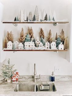 a kitchen sink under two shelves filled with christmas trees and small white houses on top of each shelf