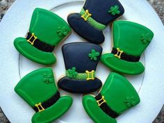 four decorated cookies in the shape of hats and shamrocks on a white platter