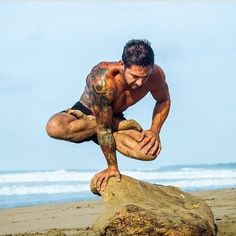 a man with tattoos on his arm and leg is leaning over a rock at the beach