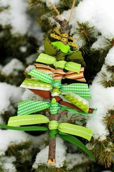 a green ribbon christmas tree ornament hanging from a pine tree covered in snow