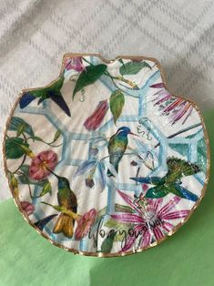 a plate with birds and flowers painted on the side is sitting on a green surface