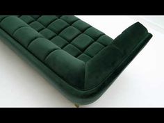 a green velvet couch sitting on top of a white floor next to a black chair