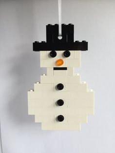 a lego snowman ornament hanging from a string on a white wall with black and orange buttons