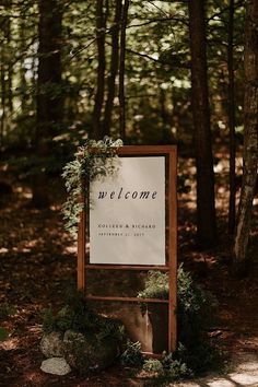 a welcome sign in the woods with greenery