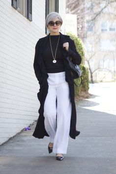 an older woman wearing white pants and black sweater is walking down the sidewalk with her purse