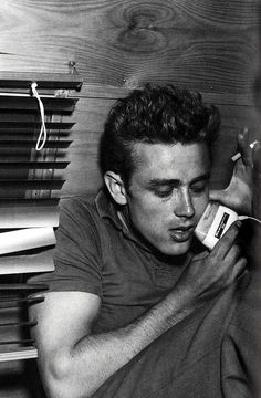 a young man sitting on the floor holding a cell phone to his ear and looking at it