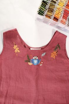 the back of a pink top with embroidered birds and leaves on it, next to colored thread spools