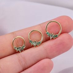 three pairs of small gold hoop earrings with green stones on each end, set in the palm of someone's hand