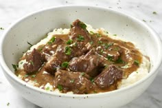 a bowl filled with meat and gravy on top of mashed potatoes