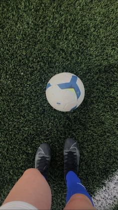 a person standing in front of a soccer ball on the grass with their feet up