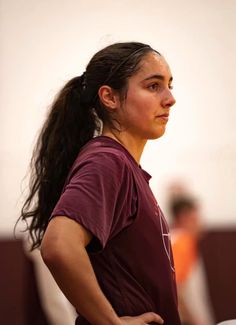 a woman standing with her hands on her hips and looking off to the side while wearing a maroon shirt