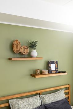 two wooden shelves on the wall above a bed in a room with green walls and pillows